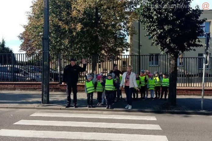 Policjanci z dziećmi na przejściu dla pieszych przed szkołą