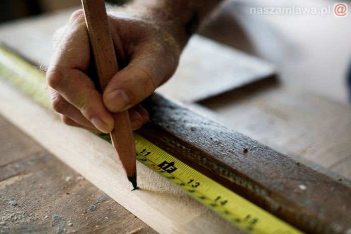 Carpenter using pencil and measurement tape on wood