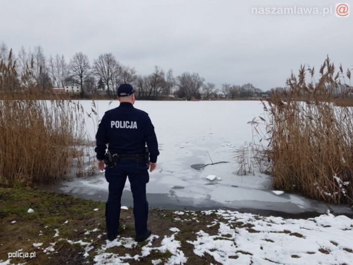 policjant przed zbiornikiem skutym lodem